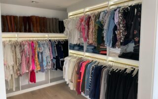 A neatly organized reach-in closet with clothes arranged by type and color on hangers, shelves with folded jeans, and tall brown boots lined up on the top shelf.