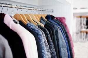 A row of assorted jackets and coats on wooden hangers hanging from a metal rod inside a closet.