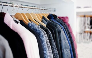 A row of assorted jackets and coats on wooden hangers hanging from a metal rod inside a closet.
