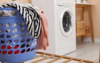 A blue laundry basket filled with clothes sits on a drying rack in front of a washing machine in a laundry room.