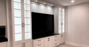 Built-in entertainment center with glass-front display cabinets, a large flat-screen TV, drawers, and overhead lighting.