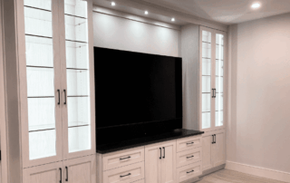 Built-in entertainment center with glass-front display cabinets, a large flat-screen TV, drawers, and overhead lighting.